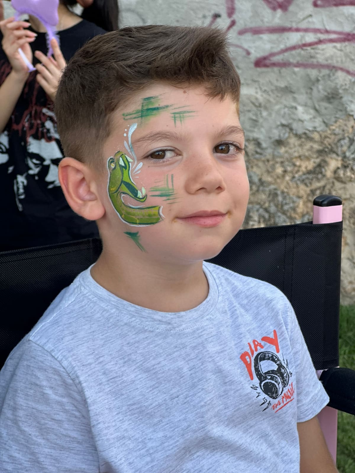 Un niño sonríe con una serpiente verde pintada en la cara