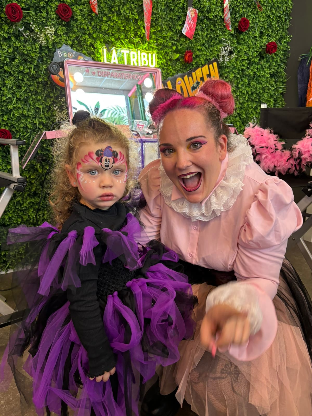 Una artista maquillada de Halloween posa junto a una niña con disfraz de tul morado y la cara pintada