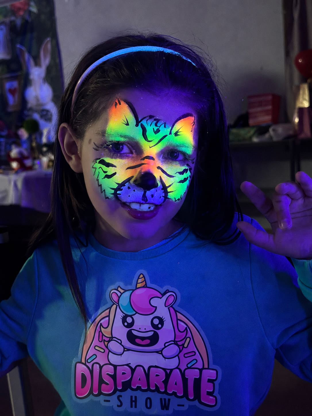 A girl with a neon tiger painted on her face, wearing a Disparate Show sweatshirt