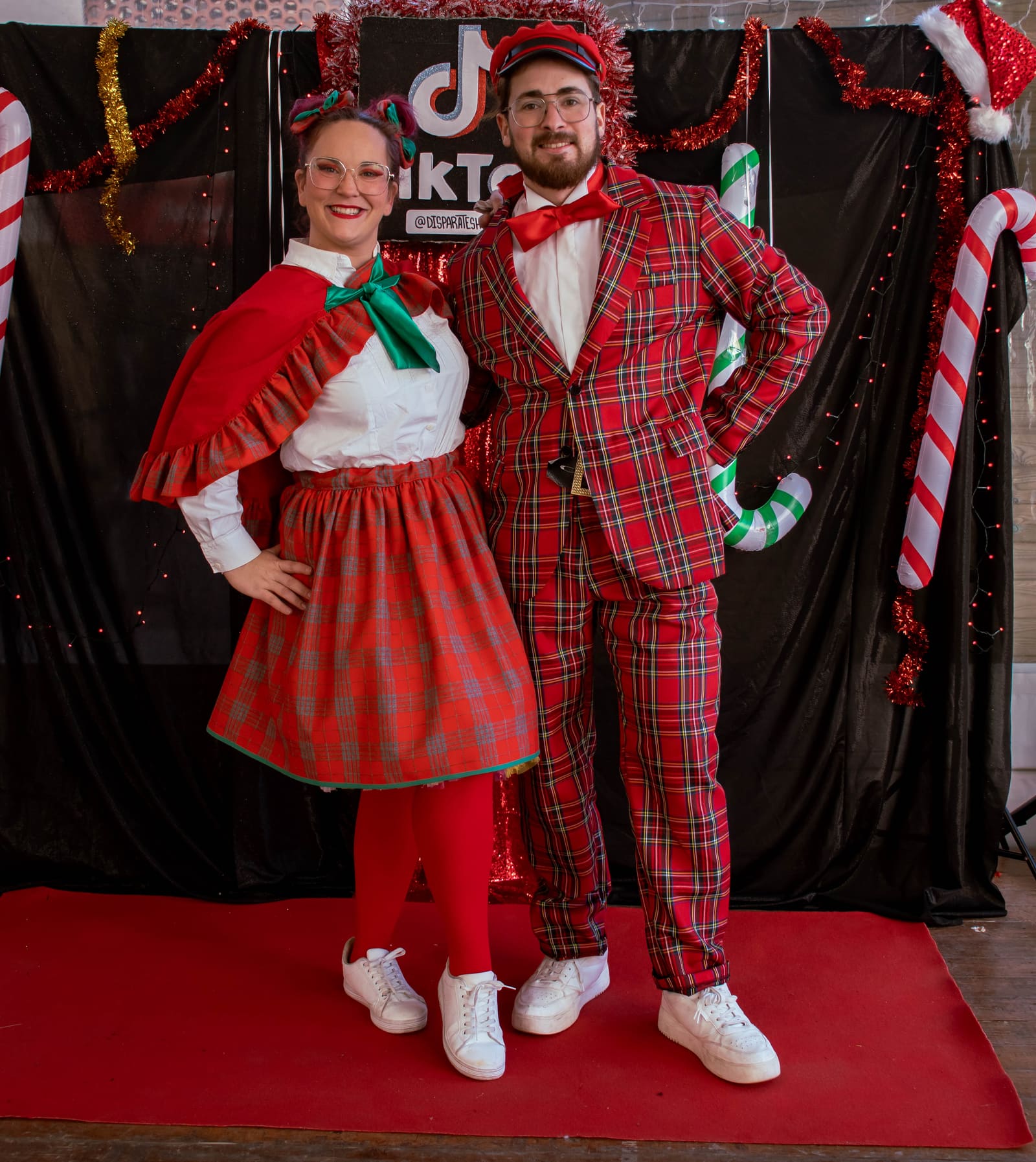 Dos personatges de Nadal, vestits de quadres vermells, posen sobre la catifa vermella