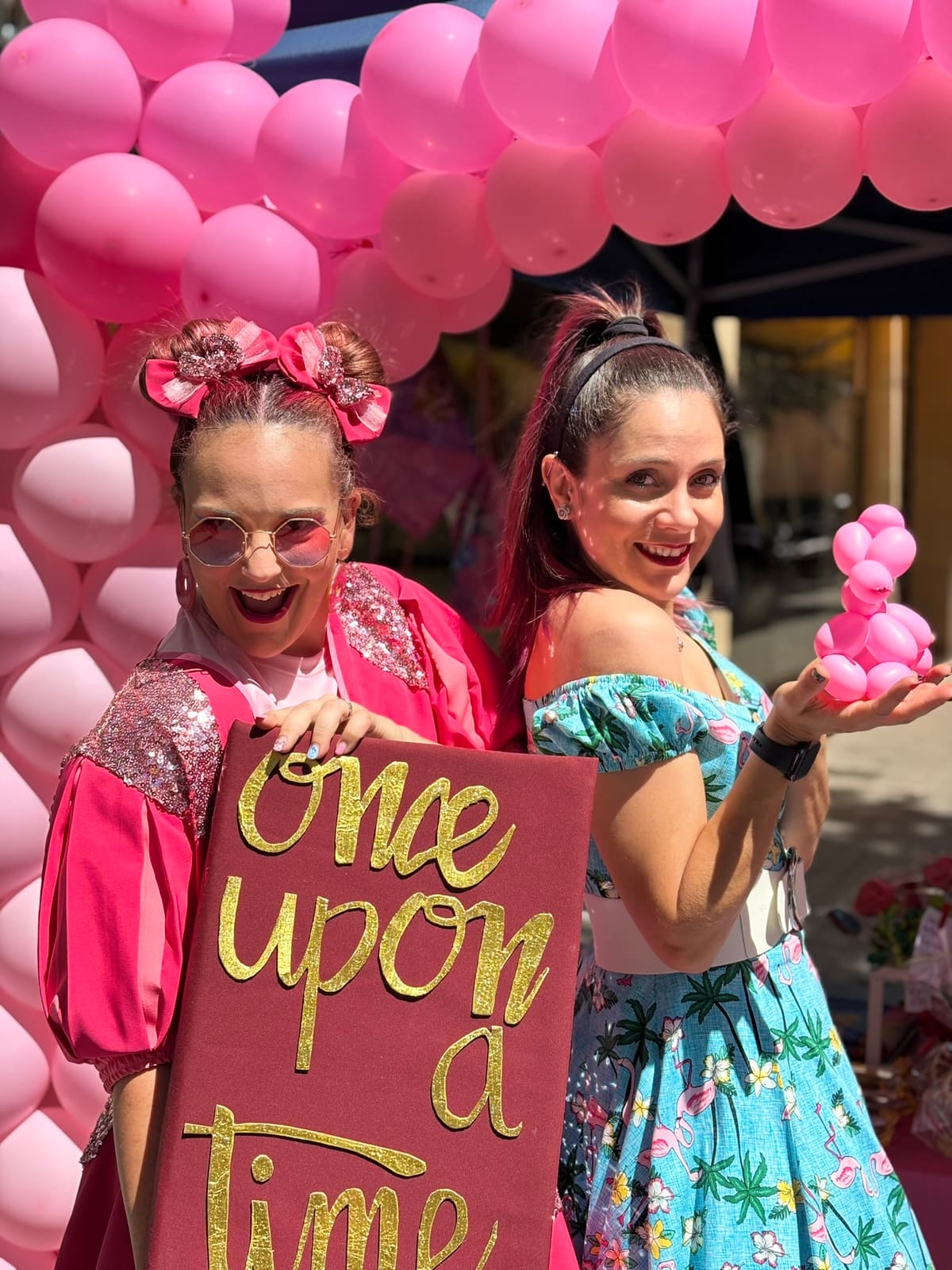 Two princesses pose among pink balloons with a fairy-tale sign