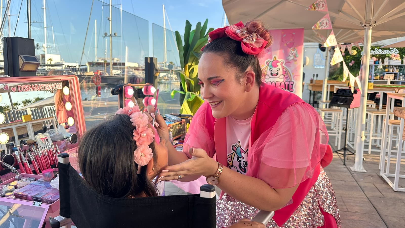 An artist does a girl's make-up in front of the corner mirror, by the harbour