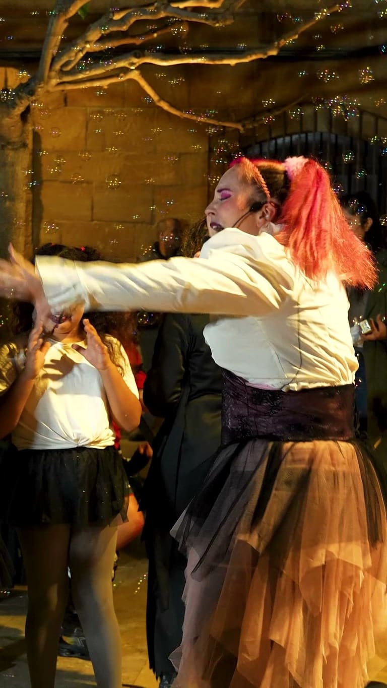 Cuca, with pink hair and a Halloween costume, opens her arms in the middle of the square during the night show