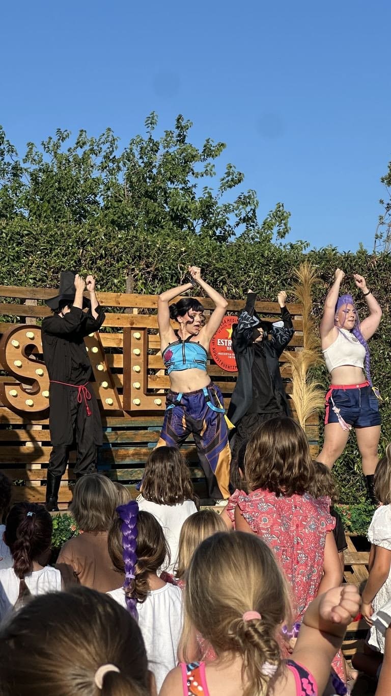 The performers with their arms in the air and an audience of girls following the routine