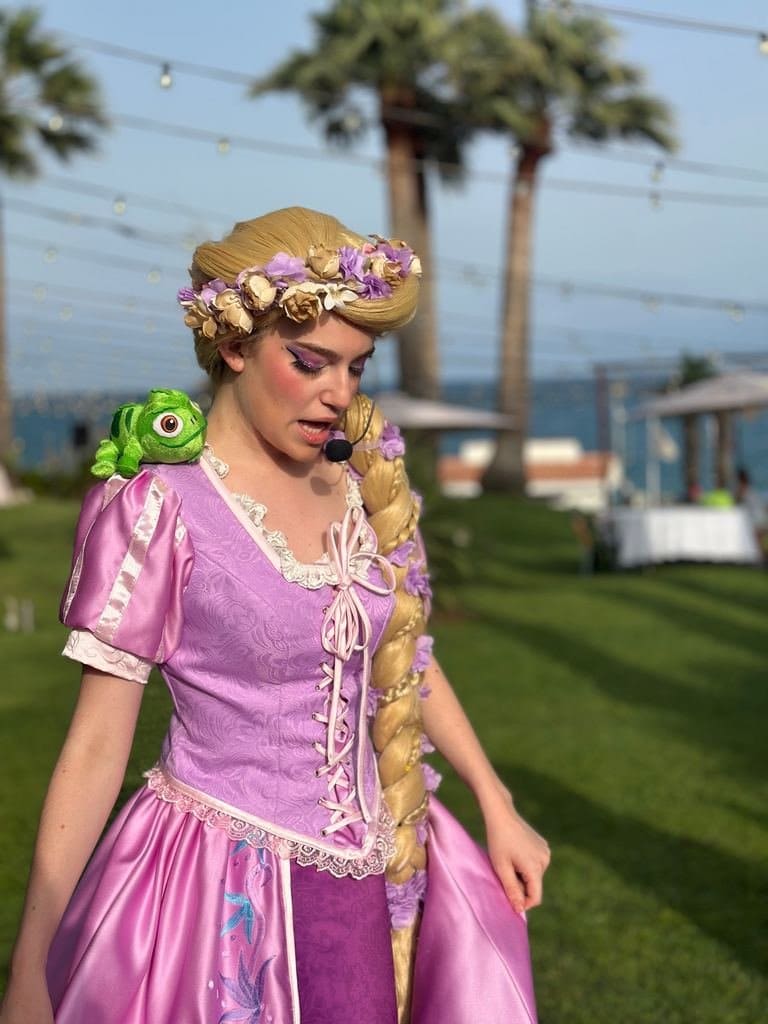 Rapunzel, her blonde braid crowned with flowers and the frog on her shoulder, on the grass