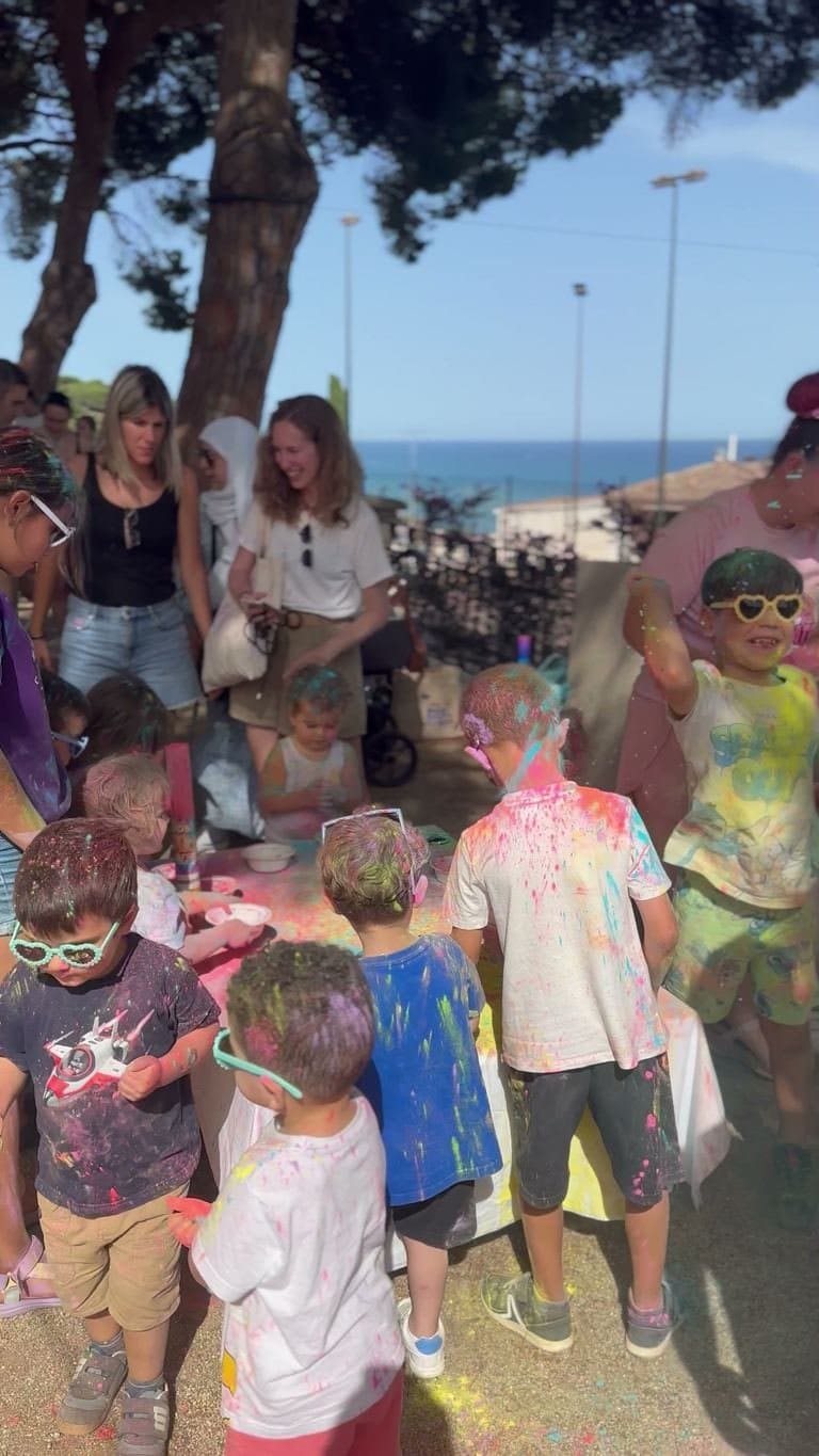 Children with their clothes dyed blue, yellow and pink next to the bowls of coloured powder